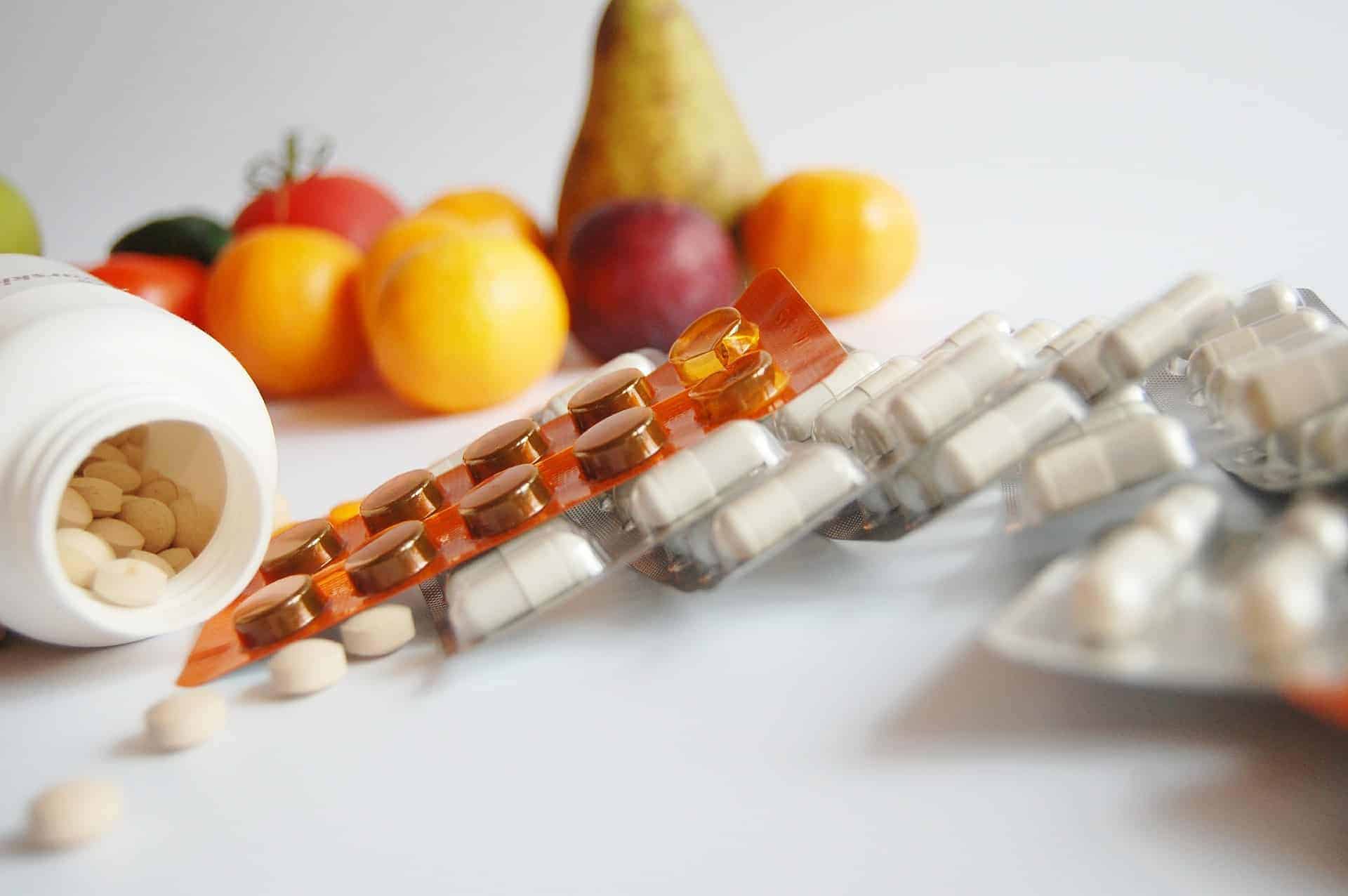 Pill bottle spilling out vitamins with food blurred in the background